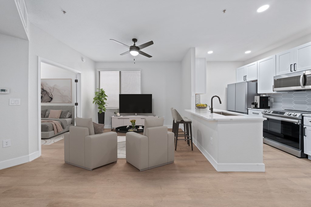 a living room with couches and a kitchen and a ceiling fan